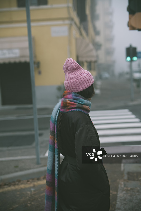 一位戴着时尚粉色帽子和配套围巾的女性正在过马路图片素材