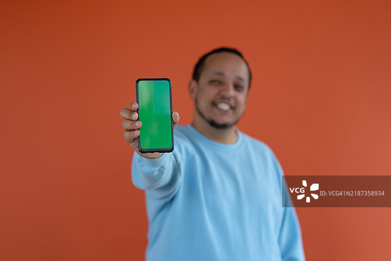 一位年轻、快乐的非裔美国男子伸出手，手中拿着一部手机，站在简单的背景前。图片素材