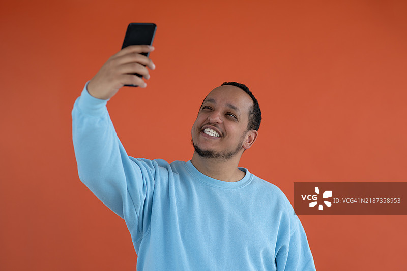 一位年轻的非裔美国男子在简单的背景前微笑自拍。图片素材