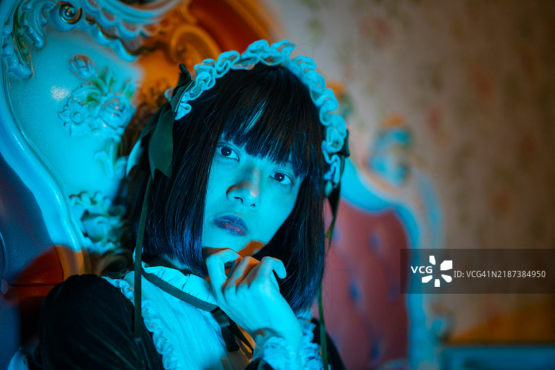 穿着绿色裙子的女人坐在昏暗卧室的床上，蓝色灯光映照着她。图片素材