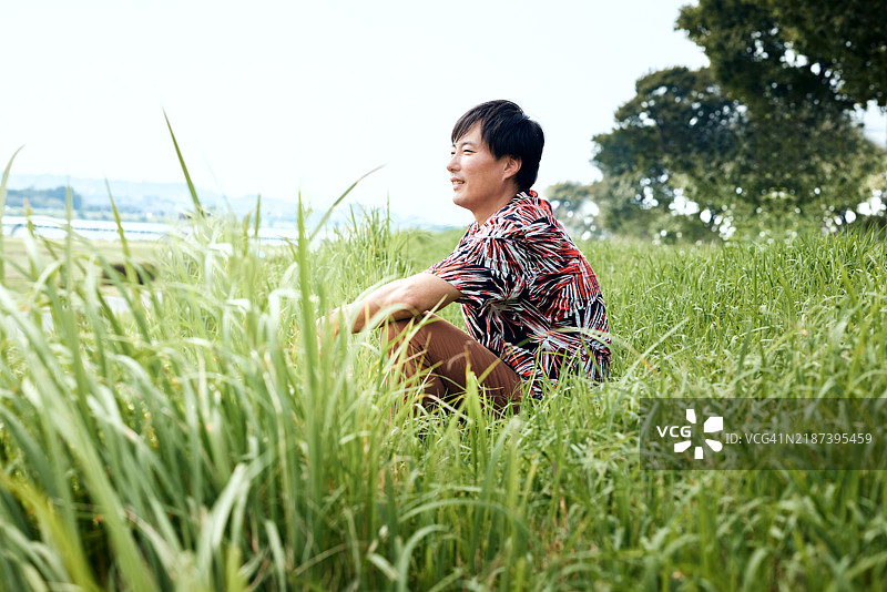 男人坐在河岸的草地上，凝视远方。图片素材