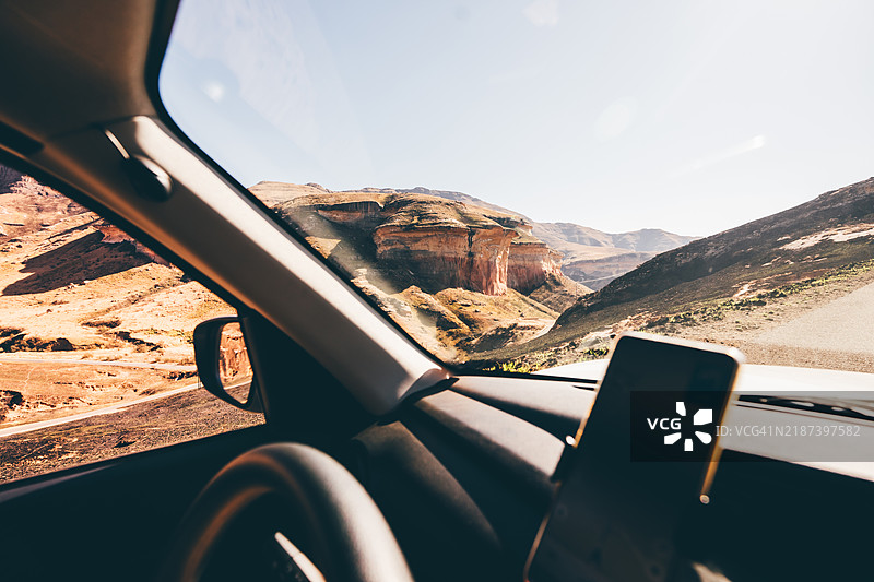 阳光明媚的公路旅行中，从车内视角看风景如画的山路。此视角强调了冒险、旅行自由以及在偏远地区使用导航技术的特点。图片素材