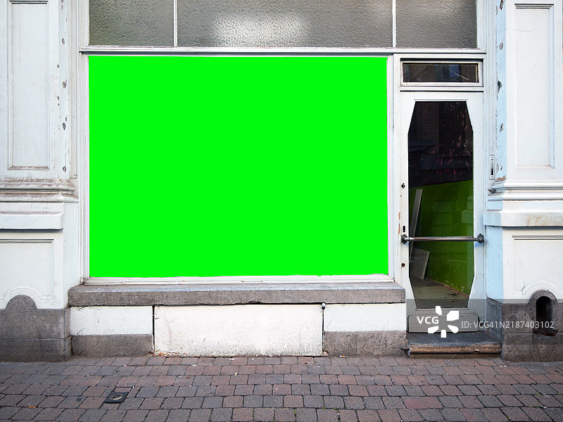 一家商店的外立面，窗户被绿色屏幕替代。复古风格的建筑。铺砌的人行道。阳光明媚。自然色彩。比利时布鲁塞尔。图片素材