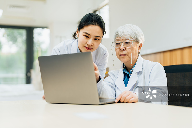 两位亚洲女性医生在医院使用笔记本电脑。医疗保健、诊所以及人们在数字平板上讨论医疗服务、结果和会议。图片素材