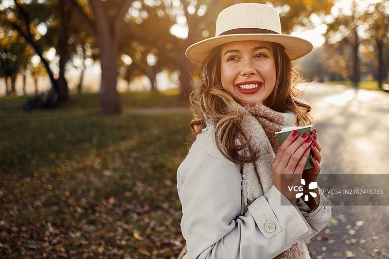 美丽的年轻女性在秋天的户外享受一杯温暖的咖啡图片素材
