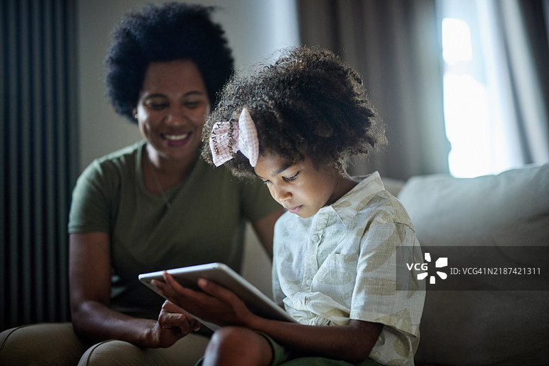 可爱的黑人女孩在家里使用触控板，身边有她的母亲。图片素材