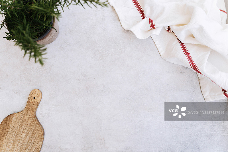 简约的平铺构图，包含一个木质切菜板、一盆迷迭香和一条毛巾图片素材