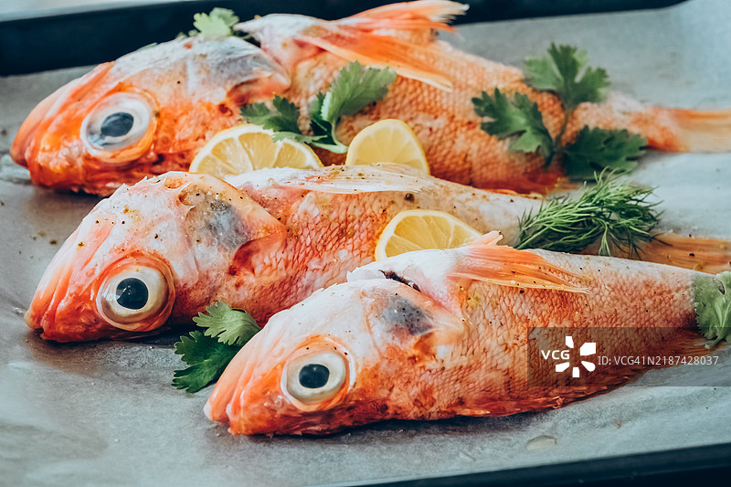 新鲜整条红鱼配柠檬和香草，放在烤盘上准备美食佳肴图片素材
