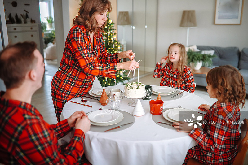 穿着睡衣的妈妈正在布置圣诞早餐桌，上面摆放着蛋糕，创造珍贵的家庭时刻图片素材
