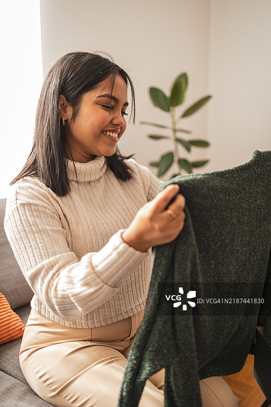 微笑的女性在家中欣赏一件舒适的毛衣图片素材