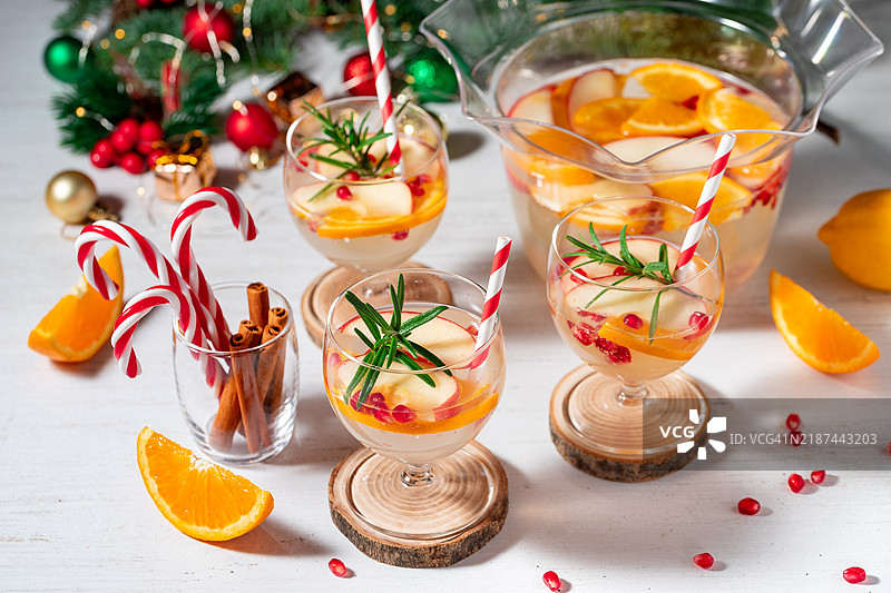 石榴圣诞红酒桑格利亚或果Punch饮品，搭配新鲜橙子、苹果和迷迭香枝，背景为圣诞装饰，留有空白空间。图片素材