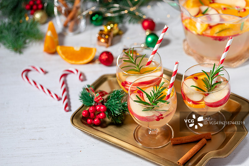 石榴圣诞红酒桑格利亚或果Punch饮品，搭配新鲜橙子、苹果和迷迭香枝，背景为圣诞装饰，留有空白空间。图片素材