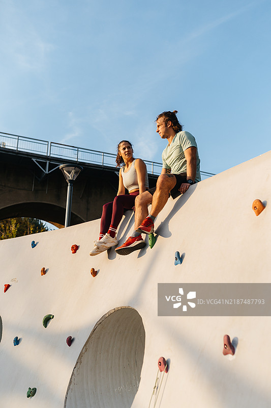 两名年轻人在户外人造攀岩墙上进行攀岩。图片素材