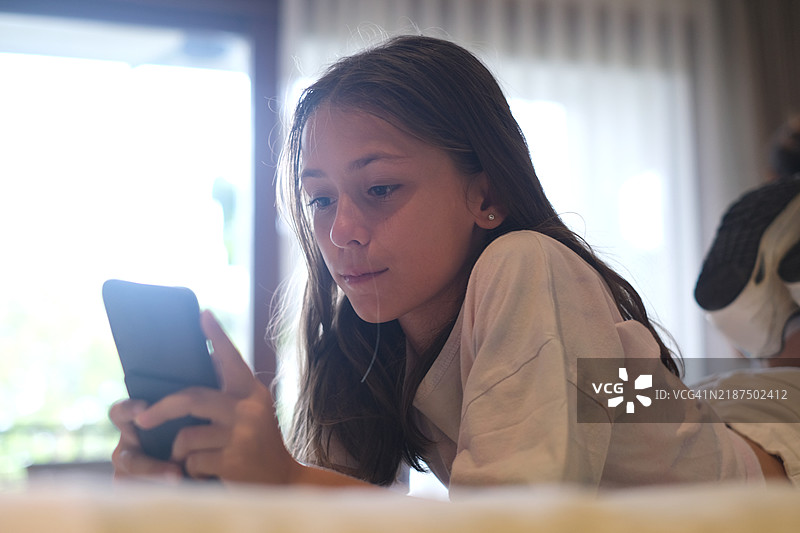 专注的少女在床上使用手机图片素材