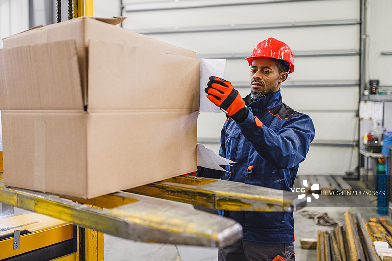 成年黑人男性仓库专员在一个酷炫的仓库里将运输标签贴在一个大纸箱上图片素材