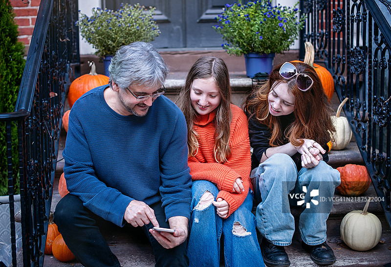 中年父亲在秋天的吉姆·索普与两个女儿聊天，一位年长，另一位年幼，坐在台阶上。图片素材