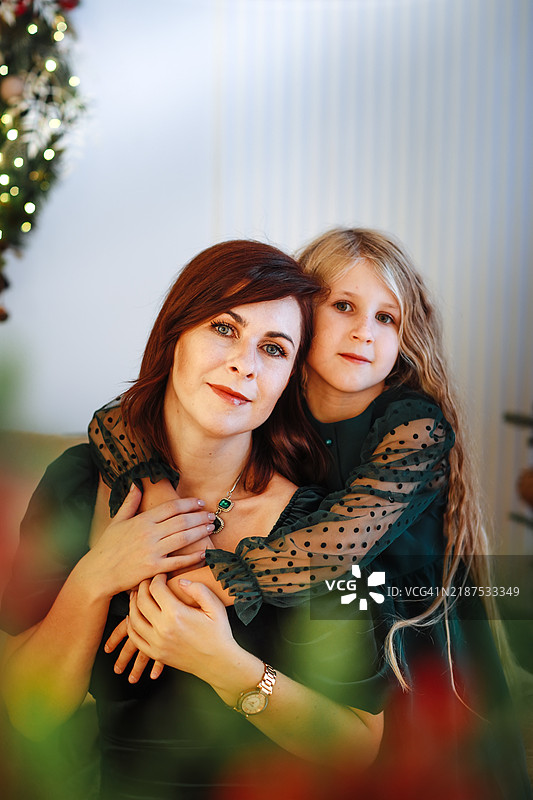 母女肖像，穿着美丽的裙子，坐在节日气氛浓厚的圣诞客厅沙发上，周围闪烁着温暖的灯光。图片素材