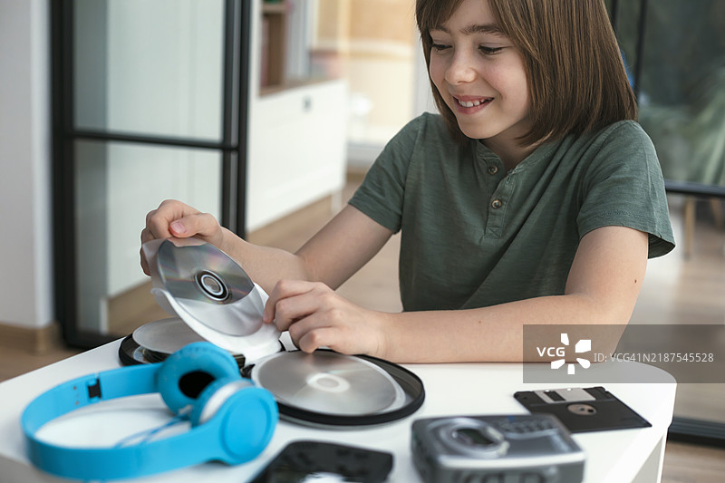 微笑的孩子在看CD或DVD、复古磁带播放器、软盘和其他老式便携设备图片素材