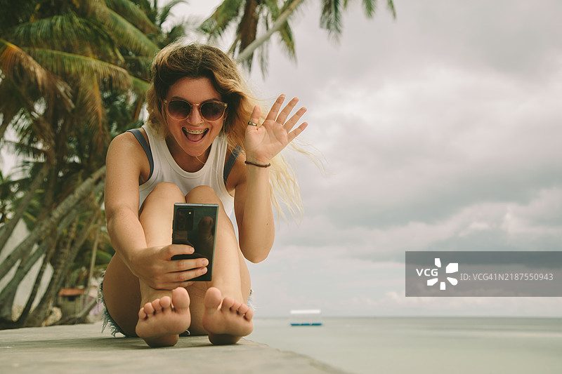 年轻女性独自旅行者在海滩上使用手机与朋友联系图片素材