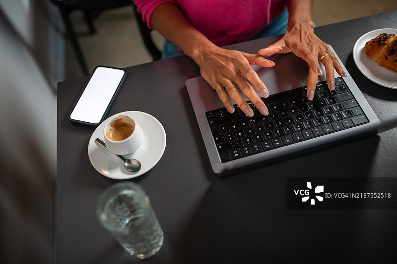 成熟的西班牙裔女性在咖啡桌前工作图片素材