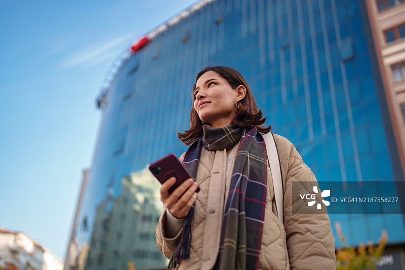 女性在城市街道上使用手机。图片素材