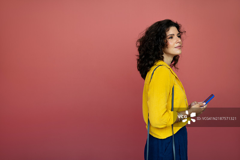 自信的女性在鲜艳的珊瑚色背景前拿着手机图片素材