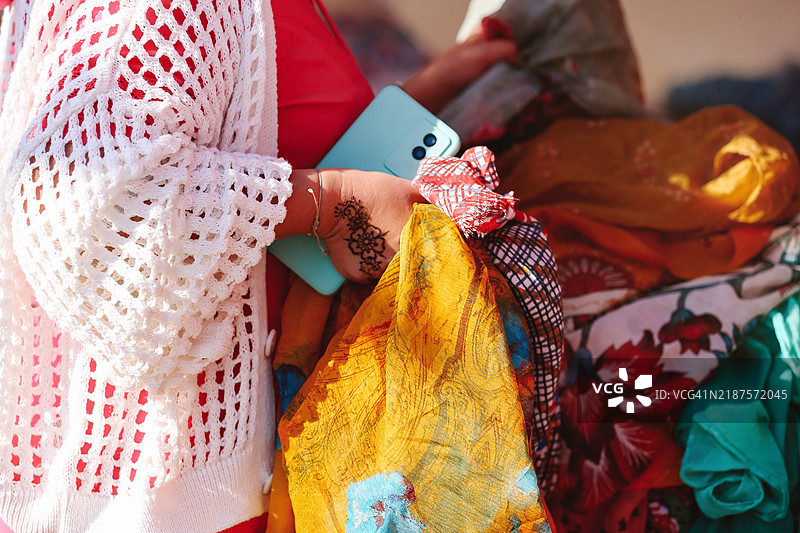 中年女性在阳光明媚的夏日街头跳蚤市场挑选色彩斑斓的披肩图片素材