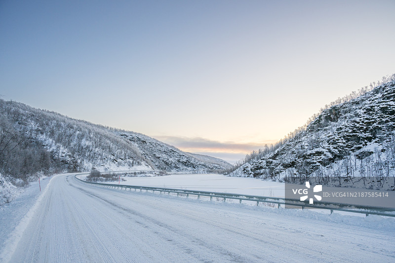 被雪覆盖的道路旁边是冰冻的湖泊图片素材