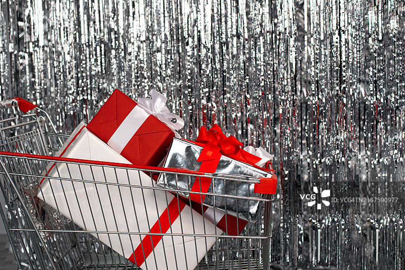 银色背景上的购物车与礼物。礼物和梦想的清单。新年。圣诞节。冬季假期和庆祝活动。折扣。促销。图片素材
