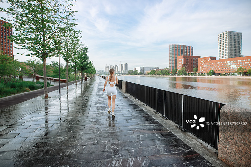 充满力量的奔跑：一位佩戴假肢的女性在繁忙的现代城市滨水区慢跑。背影和留白空间。图片素材