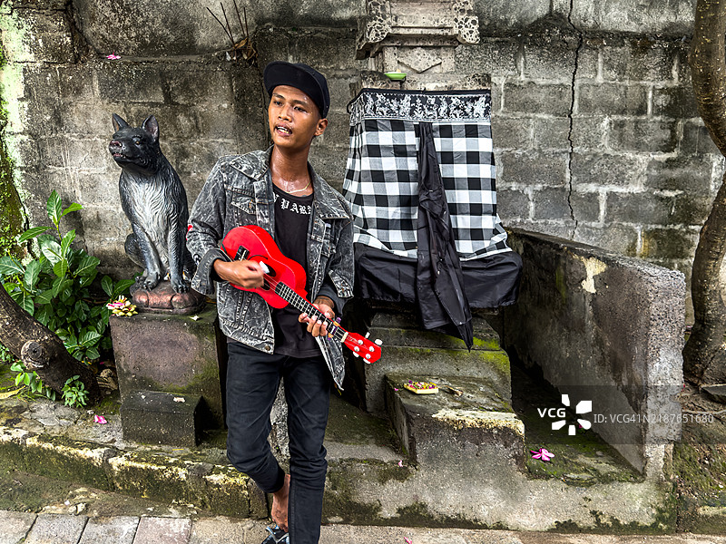 一位年轻音乐家在巴厘岛库塔海滩附近弹奏红色尤克里里。图片素材