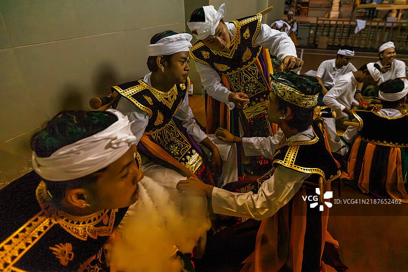 一名巴厘岛男子在印尼巴厘岛的乌布皇宫与他人一起准备庆祝活动时，吐出一团烟雾。图片素材