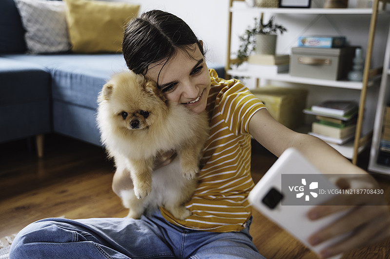 女孩在家里抱着毛茸茸的狗狗自拍图片素材