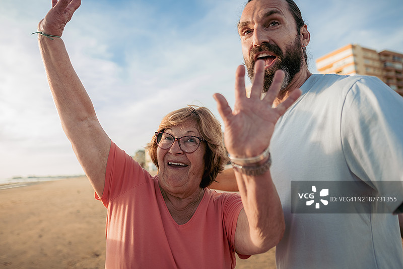 快乐的老年女性和中年男性在海滩上挥手致意图片素材