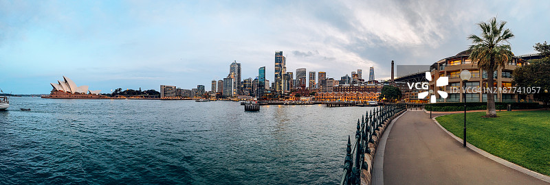悉尼港的全景，夕阳下标志性的悉尼歌剧院和环形码头，背景是城市天际线。图片素材
