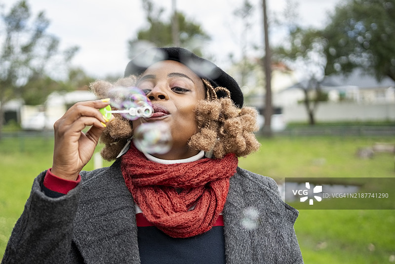 穿着温暖衣物的非洲女性在公园里吹泡泡图片素材