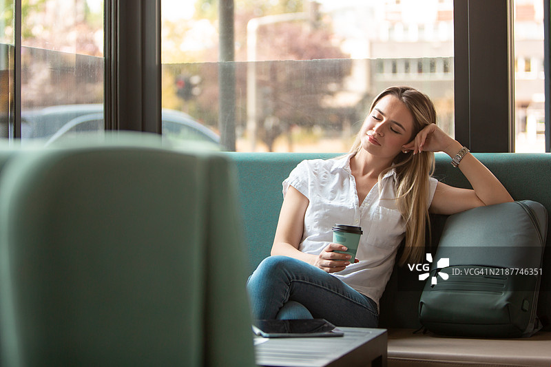 疲惫的女性在车站咖啡店等候交通时，快速小憩并喝着咖啡图片素材