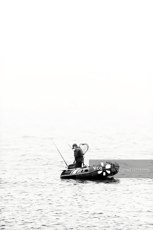 在平静的水面上从充气船上钓鱼的人图片素材