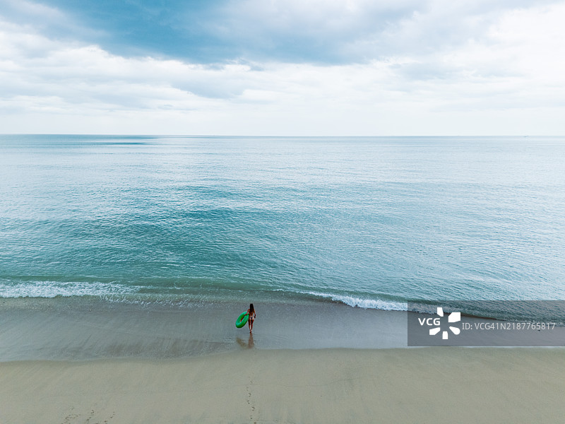女人站在沙滩上，手里拿着一个绿色的充气圈。图片素材