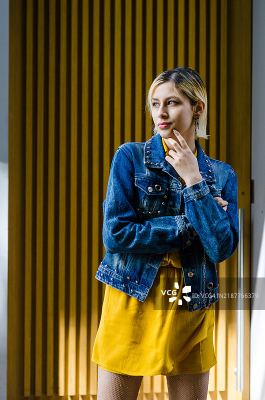 三分之三身长的快乐美丽金发年轻女性，穿着休闲服，手托下巴，站在城市街道上。图片素材
