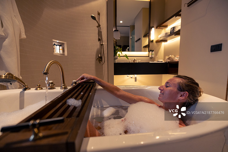 女人在泡泡浴中放松，伸手去拿香皂。图片素材