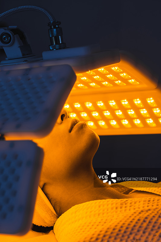 女性患者在现代奢华的美容诊所接受黄色LED光或红光治疗以实现皮肤年轻化。图片素材