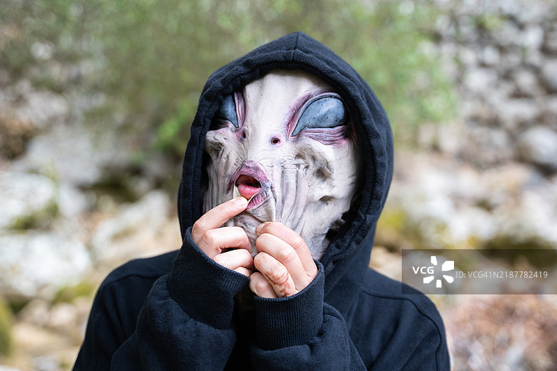 在大自然中，戴着外星人面具的人正在调整假皮肤。图片素材