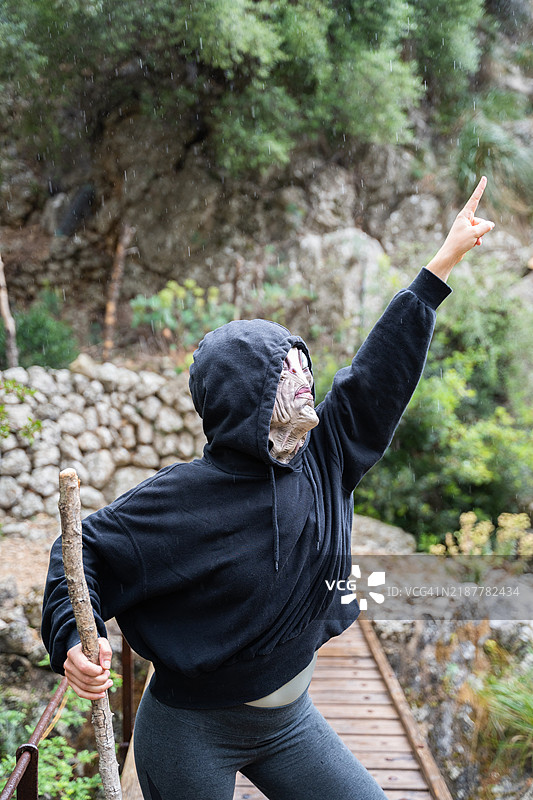 年轻女性在自然中戴着外星人面具，手指向上。图片素材