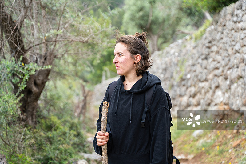 快乐的年轻女性在大自然中徒步旅行，手里拿着一根木棍图片素材