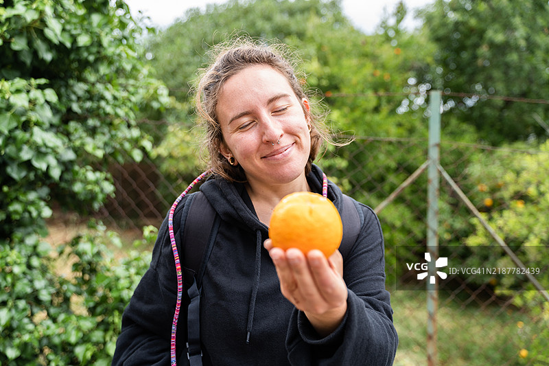 快乐的年轻女性在田野中拿着一个橙子图片素材