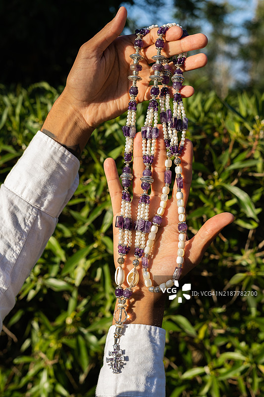 手中展示着一条美丽的紫水晶和珍珠项链，搭配银色十字架图片素材