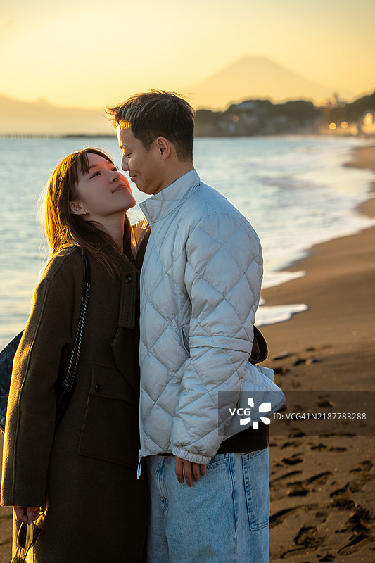 一对情侣在海边散步，背景中远处是富士山。图片素材