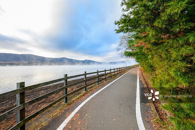 秋天的湖边小径，旁边有一座木栅栏，湖面笼罩在薄雾中图片素材