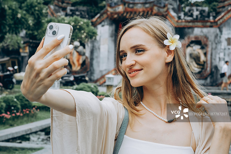 女人在越南古镇的传统背景下，佩戴花卉饰品自拍。图片素材